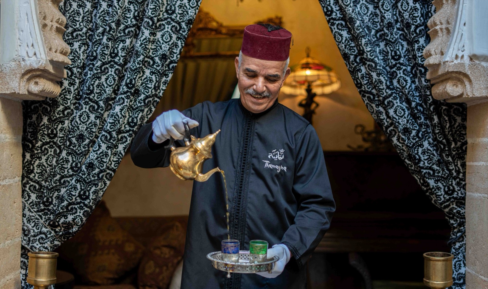 Un membre de l'équipe du riad, en tenue brodée au nom de la maison, verse le thé