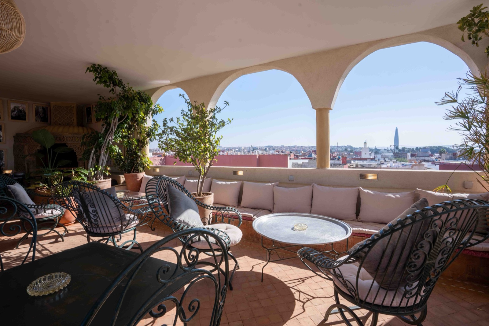 La terrasse sous arcades, fauteuils en fer forgé et banquettes, avec vue sur la ville et ses minarets